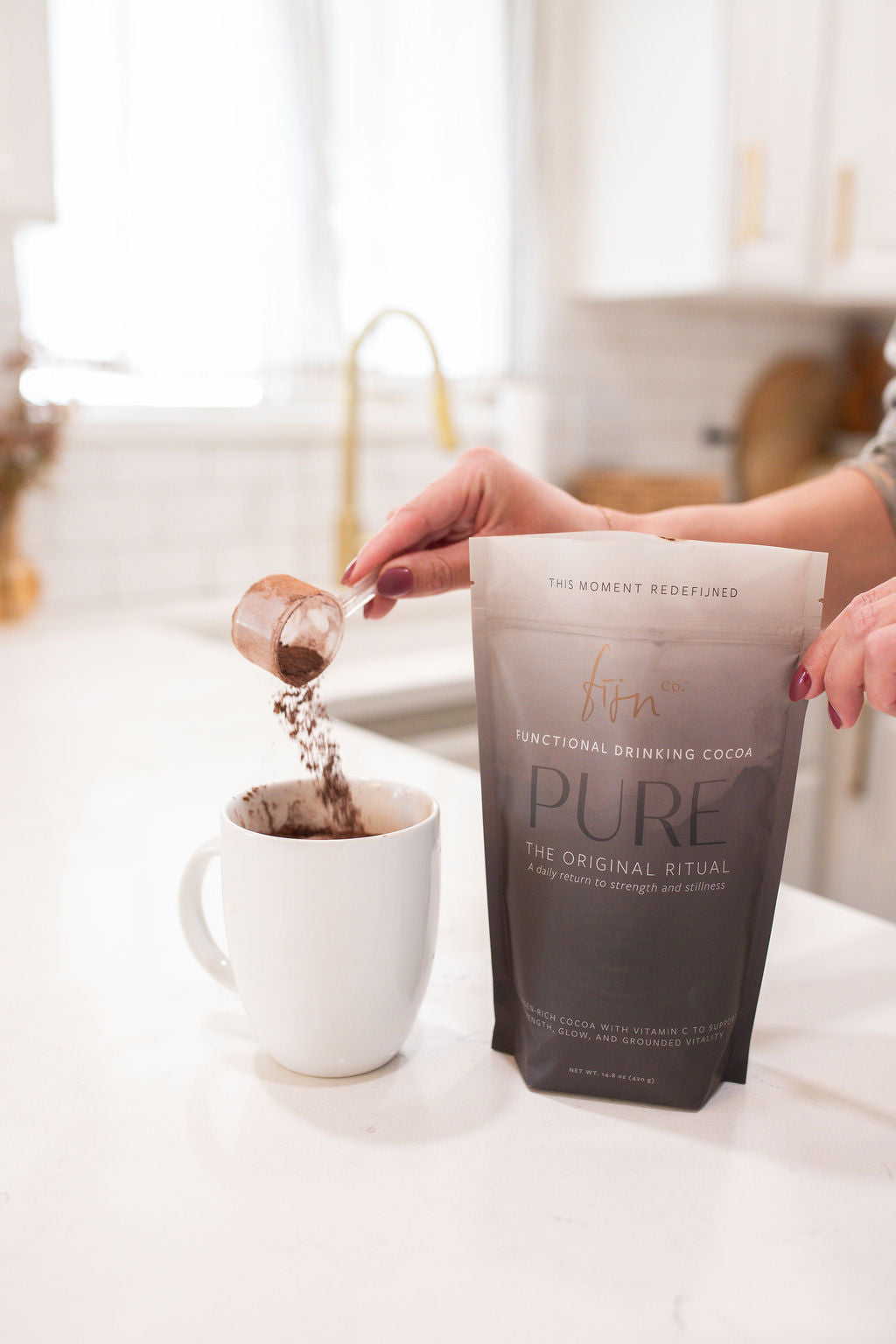 Person pouring cocoa powder a small container into a white mug with a 'PURE' product bag in the foreground.