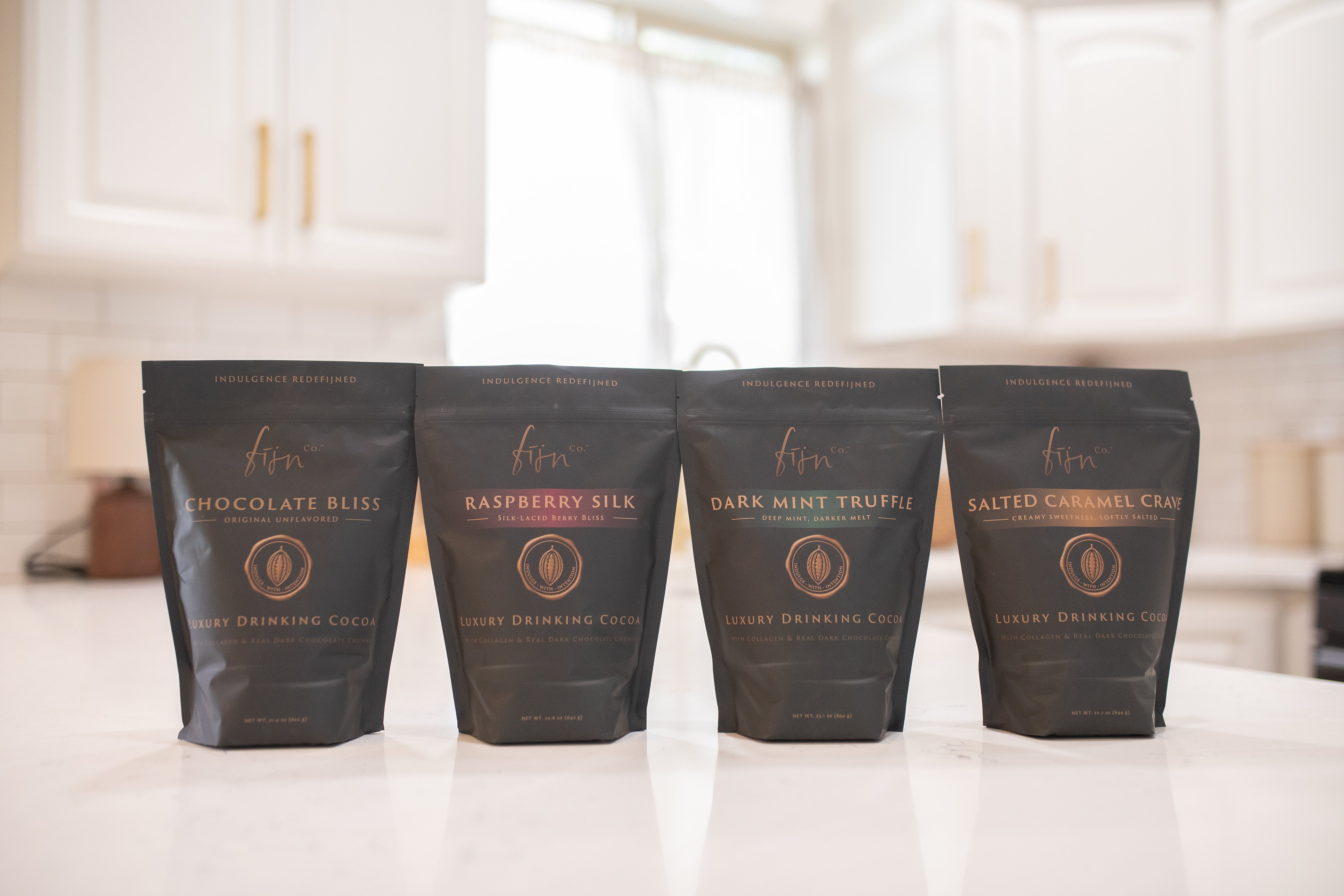 Fijn limited edition black bags — Chocolate Bliss, Raspberry Silk, Dark Mint Truffle, and Salted Caramel Crave — four small-batch sweetened cocoa blends, made once and never restocked.